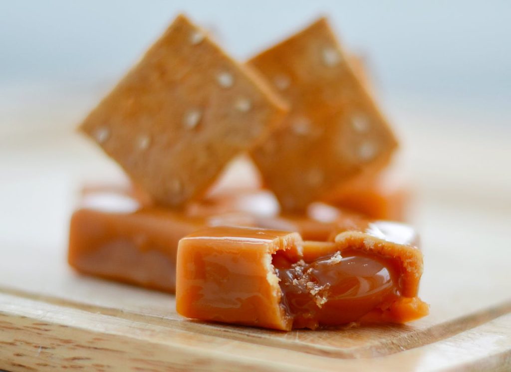 A detailed view of caramel toffee with crackers on a wooden board.